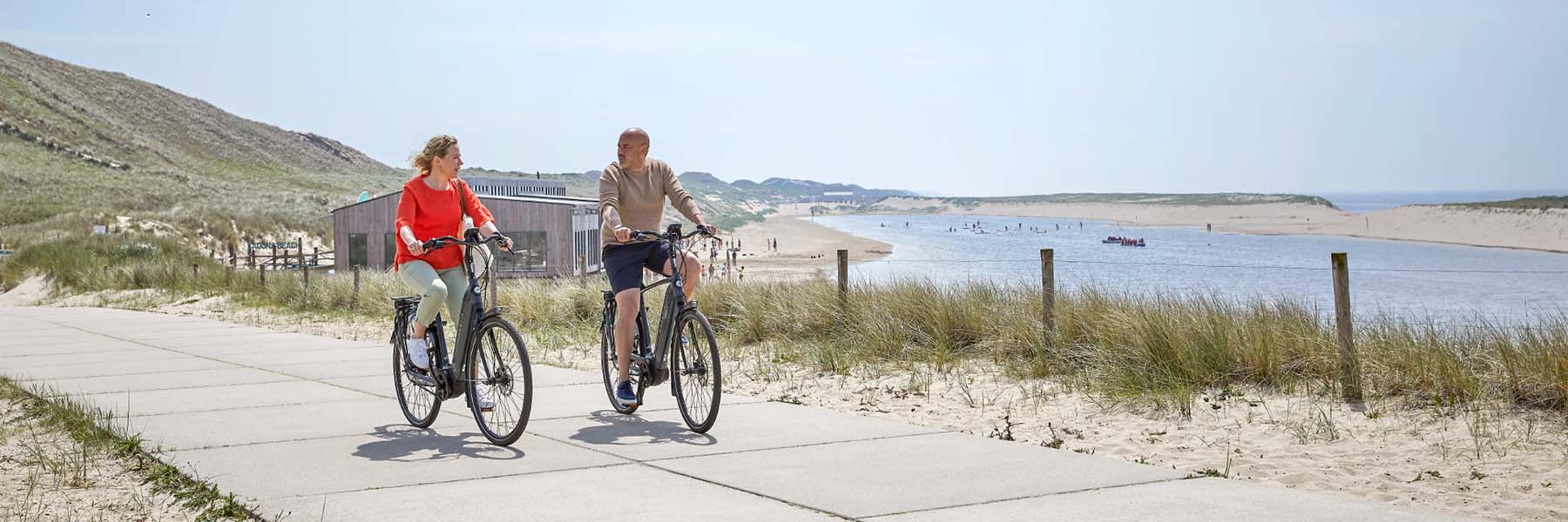 man en vrouw op grijze elektrische fiets langs het strand