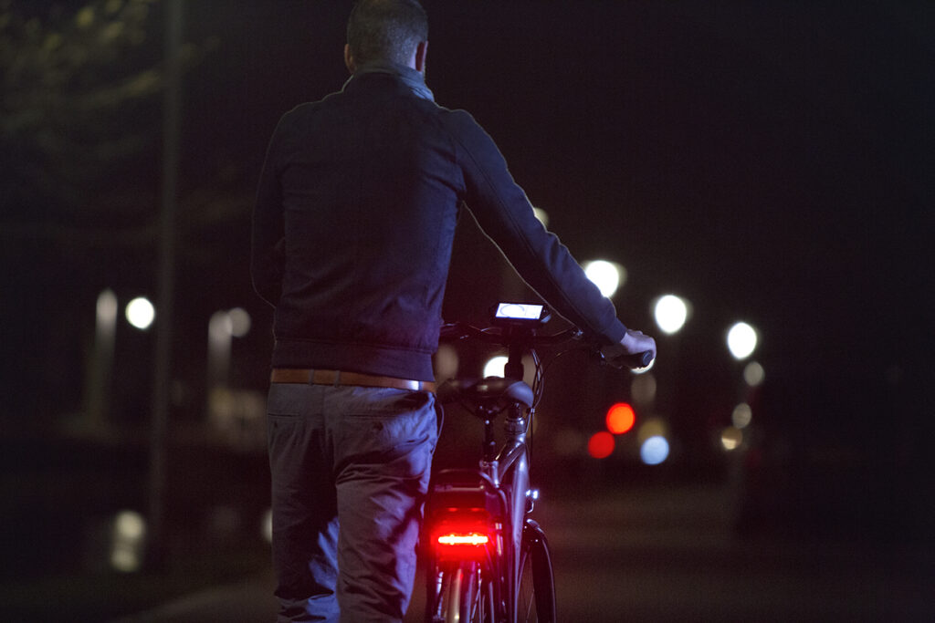 Mand går med cykel i mørket | Baglygte på cykel