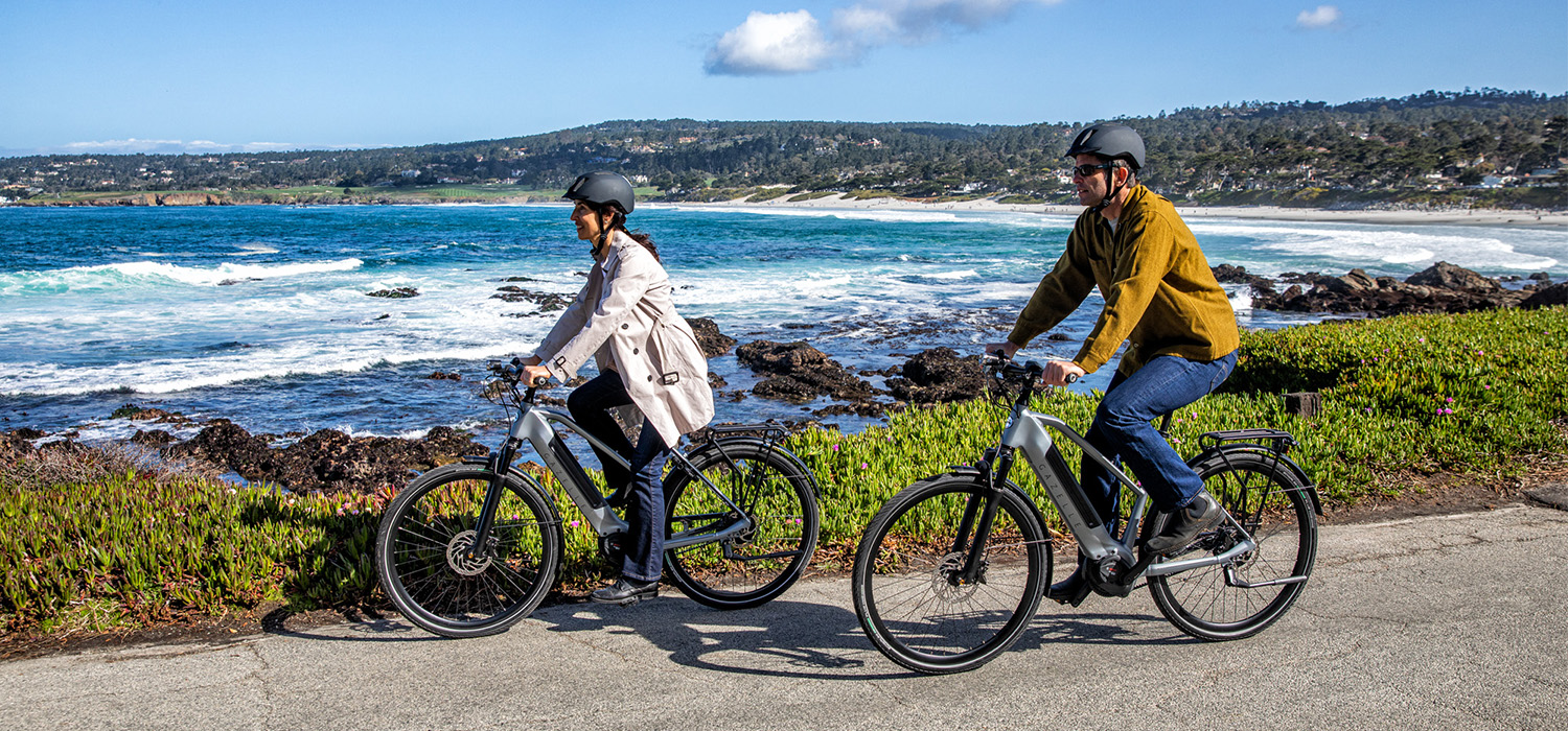 Two people riding bikes along a path next to the beach