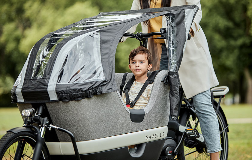 Kind im elektrischen Lastenrad mit Regenschutz